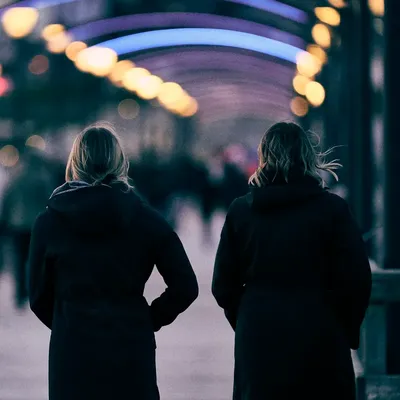 Two people walking under a lit arcade at dusk, seen from behind