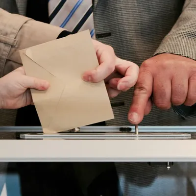 Hands dropping an envelope into a ballot box