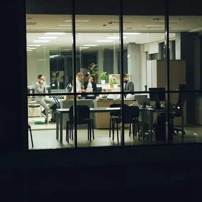 An office seen through its windows at night, a few people still at work